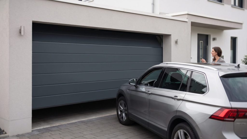 Auto steht dicht vor einer Garage, das anthrazitfarbene Sektionaltor öffnet senkrecht nach oben